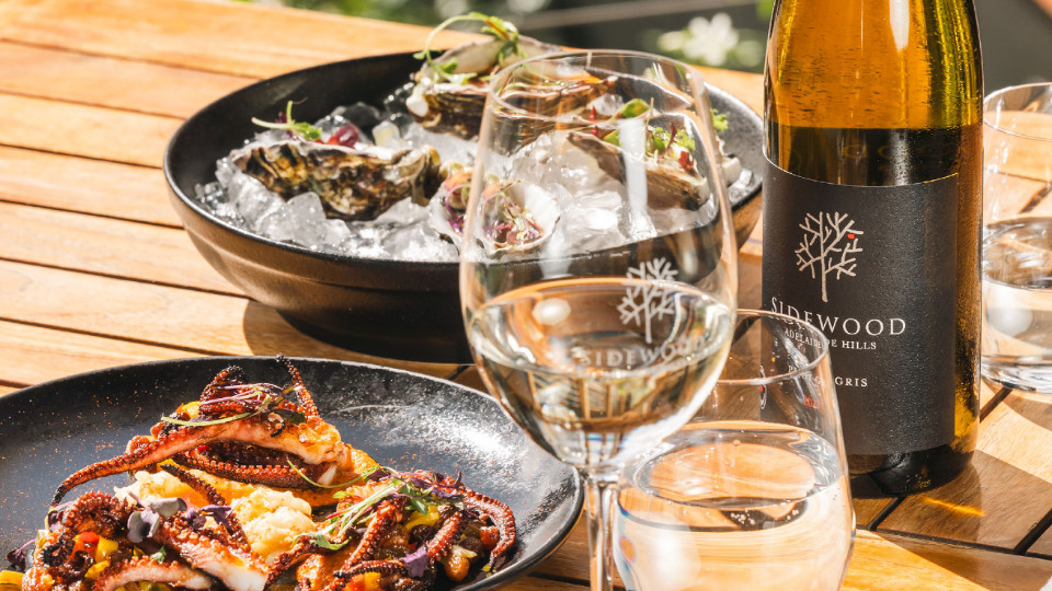 Seafood dishes, wine glasses and a bottle of wine on a wooden table.