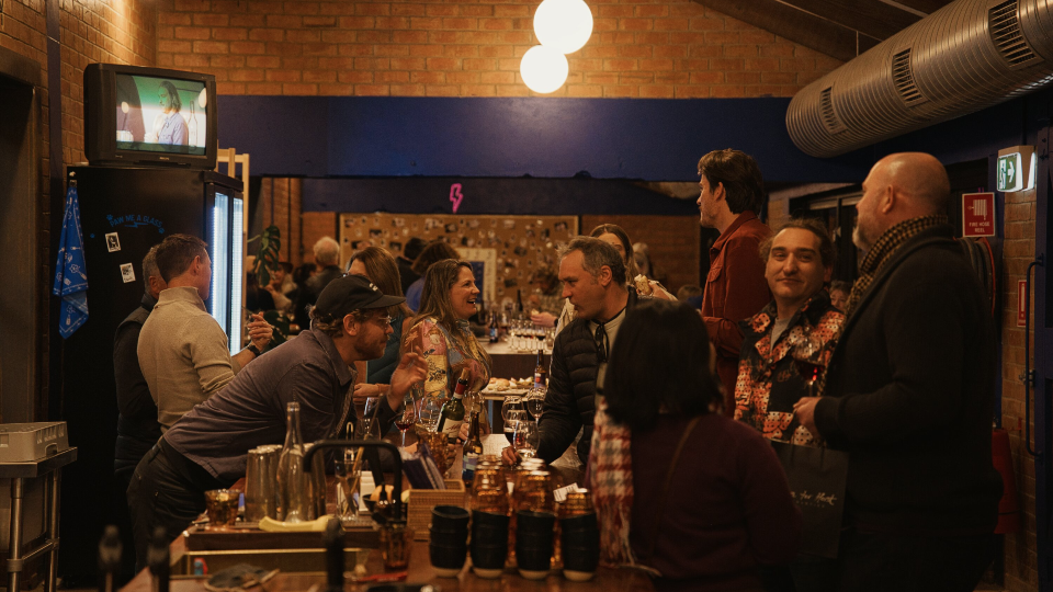 Many customers stand in a in a bar chatting over wine.